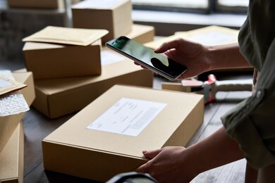 female warehouse worker seller, small stock business owner holding phone scanning retail package parcel bar code on commercial shipping box delivery order on smartphone using mobile app.