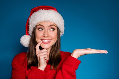 photo positive girl in santa claus hat hold hand demonstrate x-mas newyear advert promo touch finger teeth wear warm winter season clothes isolated blue gradient color background