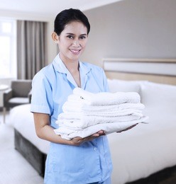 smiling young cleaning lady holding towels shooting at hotel room