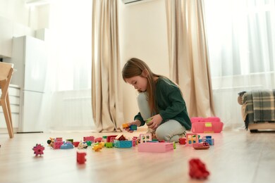 a little girl holding a couple of toy bricks playing alone in a middle of a bright room at home