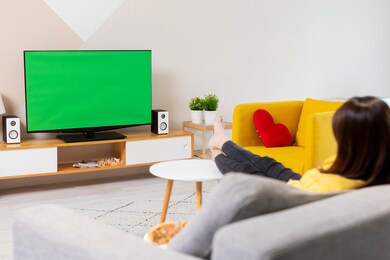 side of asian young woman watching green chroma key screen tv on the sofa at home with food alone