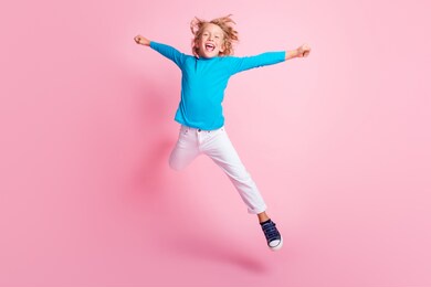full length photo of small boy jump star pose wear blue turtleneck pants sneakers isolated pastel pink color background
