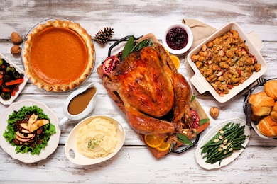 classic thanksgiving turkey dinner. overhead view table scene on a rustic white wood background. turkey, mashed potatoes, stuffing, pumpkin pie and sides.