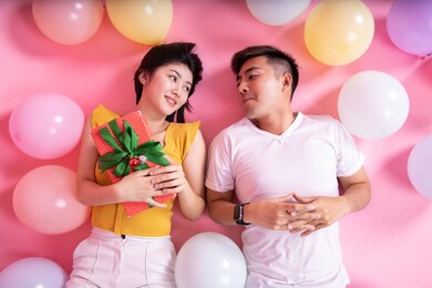 couple in love.asain woman surprising his boyfriend with a gift. young woman on birthday holiday party. celebrating with pastel color balloon.