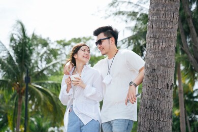 asian couple traveler holding shoulder standing on the beach near coconut tree.