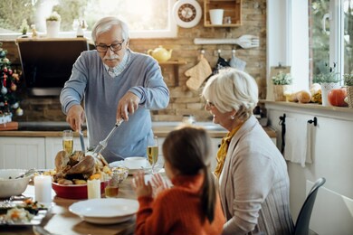 mature man serving thanksgiving turkey while having family lunch at home. 