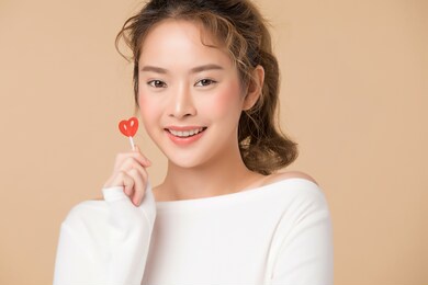 portrait of young woman holding a candy in heart shape isolated on beige color background