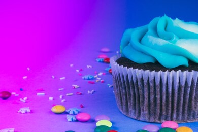 chocolate cupcake with whipped cream in a blue background, decorated with sugar snowflakes, sprinkles, colorful candies, holiday concept, greeting card, toned in trendy neon