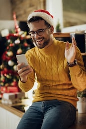 young happy man waving while making video call over smart phone on christmas eve at home. 