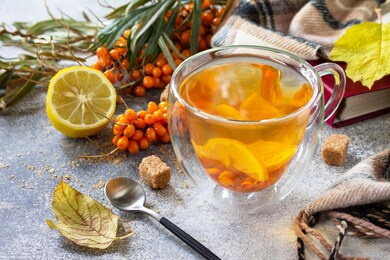 healthy autumn vitamin drink. hot sea buckthorn tea with lemon with fresh sea buckthorn berries on a stone countertop.