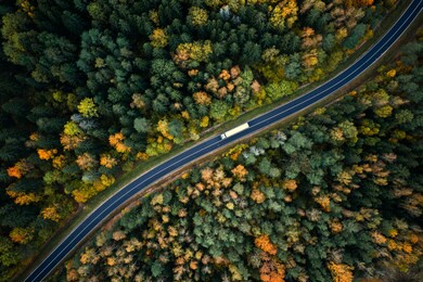 arial view of heavy truck on a narrow twisting road. autumn colorful trees by the sides of the road.