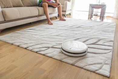 robotic vacuum cleaner works on the surface. indoor cleaning auomate. latest technology. young man is controlling the robot vacuum cleaner by its app.
