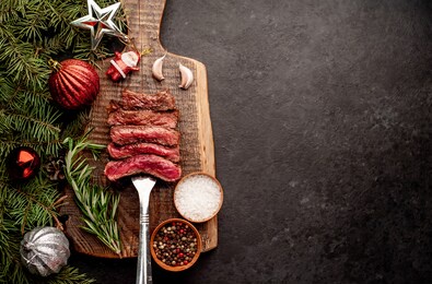 
different degrees of roasting of steak on a meat fork for christmas on a background of a stone with a spruce and christmas toys with copy space for your text