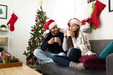 happy latin couple relaxing and enjoying christmas together drinking hot chocolate and staying warm at home