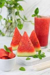 buah semangka or watermelon fruit, cut on wooden white chopping board, with a bowl of slices watermelon and watermelon juice. bright mood photo on white marble background.