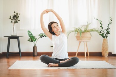 smiling healthy asian woman doing yoga shoulder stretching at home in living room