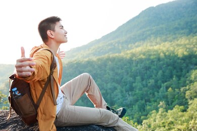 asian teenager sitting on cliff bridge edge and looking at the mountain.
