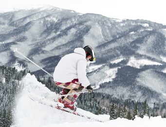 winter kinds of sport concept. back view of skier wearing ski suit and ski equipment doing jump trick in winter season. entertainments at ski resort in the mountains, copy space