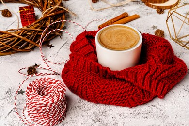 coffee mug in a soft red winter scarf on a gray background with christmas decorations. christmas coffee break for home recreation. the view from the top