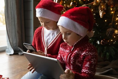 small caucasian boy and girl children look at gadget screens play computer online games on winter holidays at home. little brother and sister kids engaged in digital virtual activity on devices.