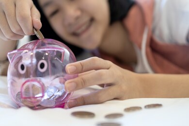 close up of a coin in the hand,smiling asian child girl putting coin into piggy bank,feel happy,saving money for the future in education,health care and medical insurance,concept of financial planning