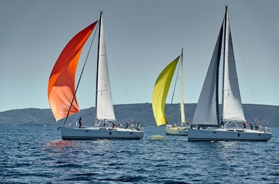 sailboats compete in a sail regatta at sunset, race of sailboats, reflection of sails on water, multicolored spinnakers, number of boat is on aft boats, island is on background, clear weather