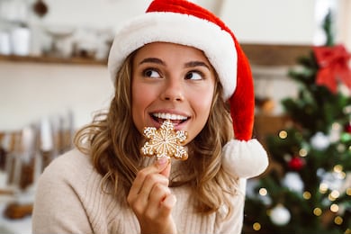 happy cute woman in santa claus hat smiling and eating christmas cookie in cozy kitchen