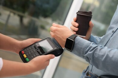 man using smart watch for contactless payment via terminal in cafe, closeup