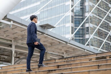 confidence asian businessman office worker in suit holding digital tablet and walking up the stairs at railway station in working day. transportation, technology and financial business concept.
