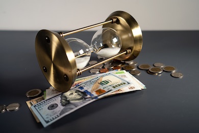 gold hourglass with hundred us dollars banknotes with coins isolated on grey table. selective focus. business and investment concept. financial crisis. loan.