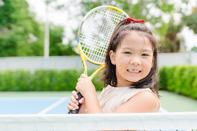 little tennis player play tennis in court on summer.confident asian child girl lose fist tooth with big smile she holding racquet for training ready to play tennis with trainer coach in sport club.