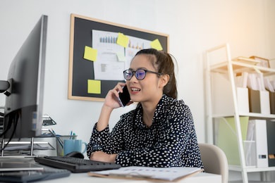 young asian business women talking on mobile phone while working on laptop at desk office
