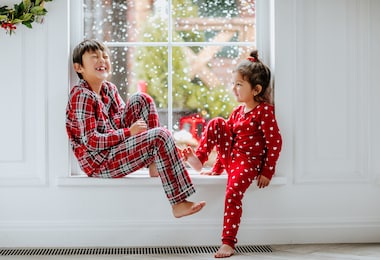 young asian pretty girl and boy in red pyjamas in red hearts posing on the big window with snow background. high quality photo. high quality photo