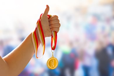woman hand raised with a thumb up sign, holding gold medal. award and victory concept, copy space for text. first place in competition