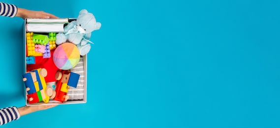 donation concept. kid hands with donate box with clothes, books and toys on light blue background. top view