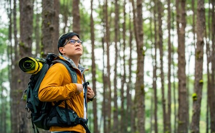 portrait of handsome asian man hiker hiking with backpack in autumn forest. male backpacker relax and enjoy walking alone on mountain trail. healthy outdoor lifestyle holiday vacation concept.