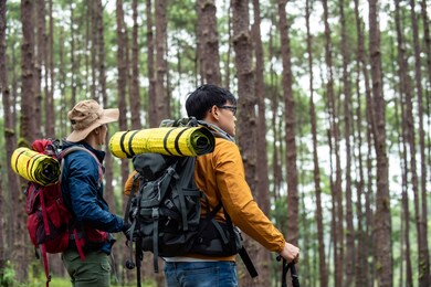 portrait of two asian man friends hiking together in autumn forest. male backpacker walking on mountain trail. healthy outdoor lifestyle, friendship and holiday vacation concept.