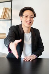 corporate deal. partnership agreement. cooperation contract. business meeting. confident cheerful chinese business man in glasses greeting customer offering hand at light workspace.