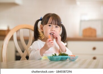young girl eating fresh green vegetables against real kitchen background