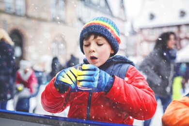 happy little kid boy in colorful warm clothes on skating rink of christmas market or fair drinking hot punch or chocolate. healthy child having fun on ice skate. people having active winter leisure