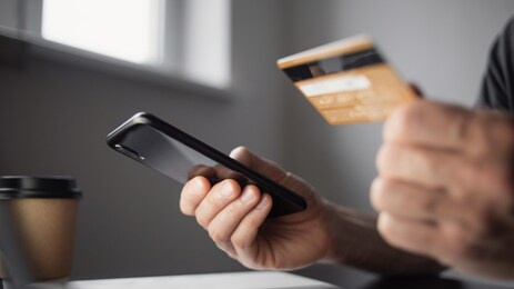 man holding credit card and using smartphone at home
