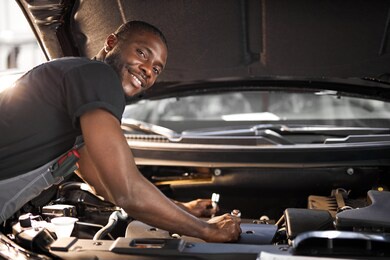 handsome guy repairing auto's hood, using tools. wearing unifrom, concentrated on work