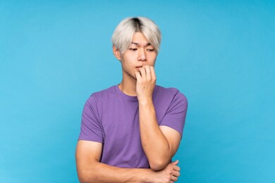 young asian man over isolated blue background having doubts