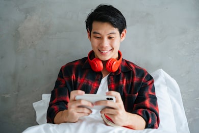 asian young man enjoy playing mobile game on smartphone at bedroom.