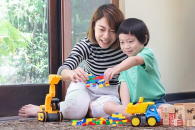 asian mother is playing block toys with son while construction car, truck and wooden abc block are on the floor. quality family time concept.