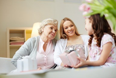 portrait of happy little girl, her mother and grandmother with giftboxes talking at home