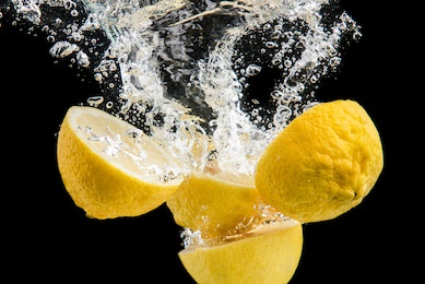 fresh yellow lemons in water splash on black background with lots of air bubbles.