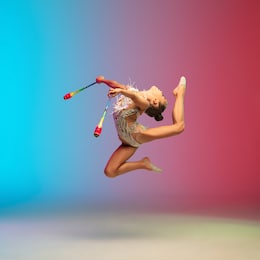 high jump. little caucasian girl, rhytmic gymnast training, performing isolated on gradient blue-red studio background in neon. graceful and flexible, strong child. concept of sport, motion, action.