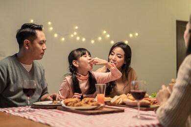 asian young little girl enjoy eating her meal crispy fried chicken together with family in christmas and new year party. the kid feeling happy to stay with parents and grandparents during holiday.