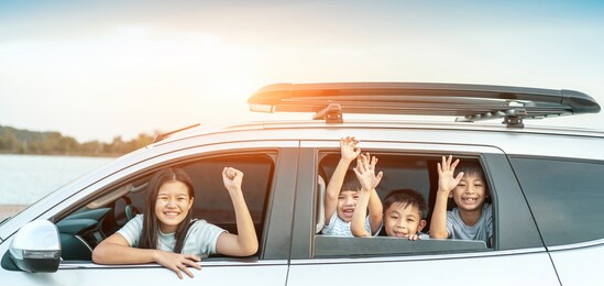 happy kids travel by the car, little boy peeks out of the car in the sunset. happy siblings waving hands travel by car against blue sky. summer road trip concept